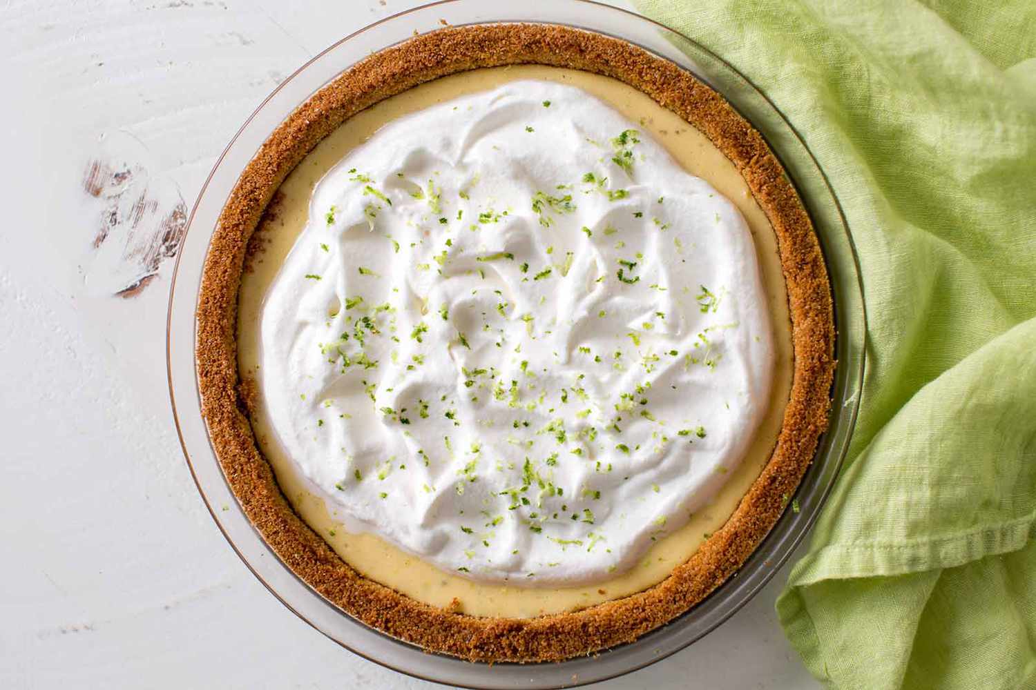 Overhead shot of a homemade keylime pie, covered with whipped cream and with a linen beside