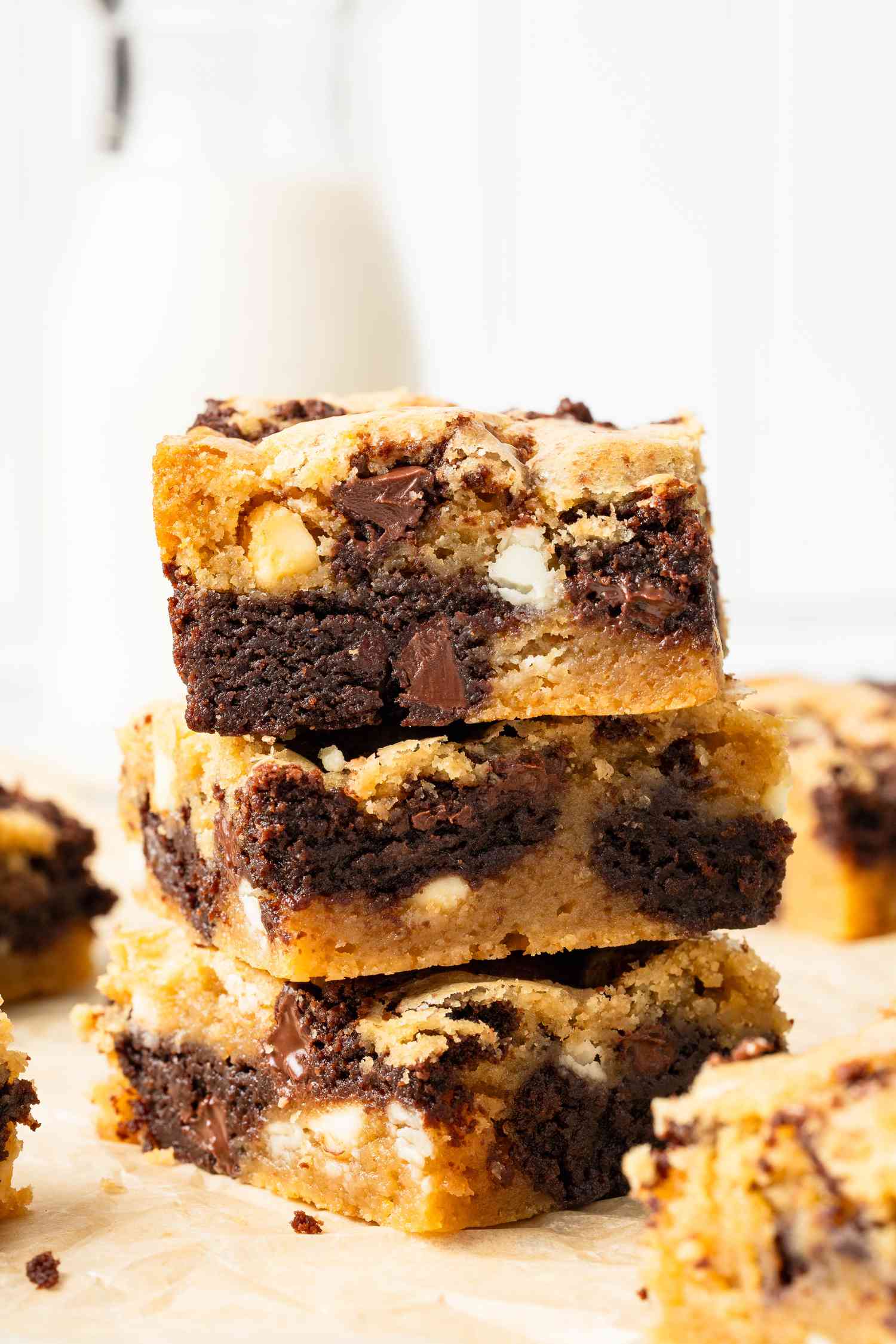 Stack of slices of marble brownies on a piece of parchment paper, and on the counter surrounding the stack, a carafe of milk and more slices of the brownies